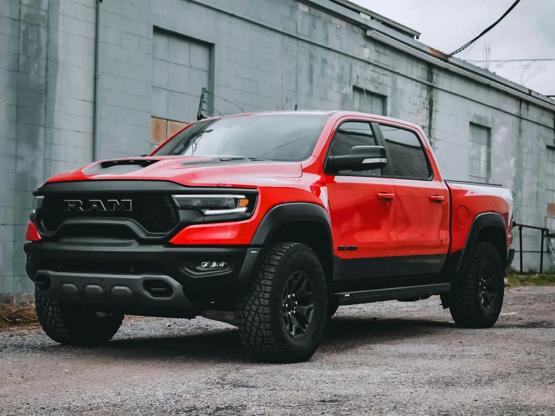 Red Ram TRX truck parked in front of a gray industrial building.