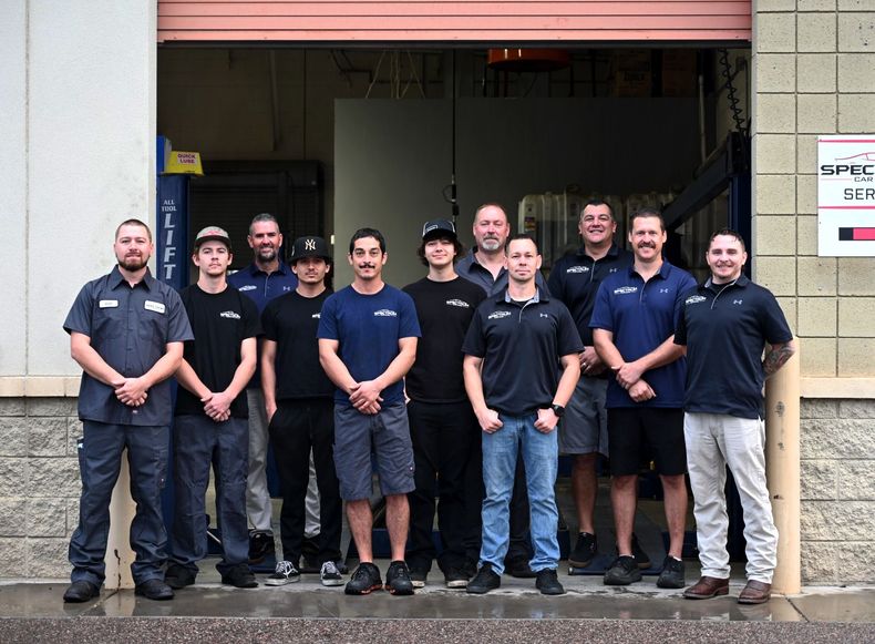Group of eight people in navy work uniforms standing outside a garage bay entrance
