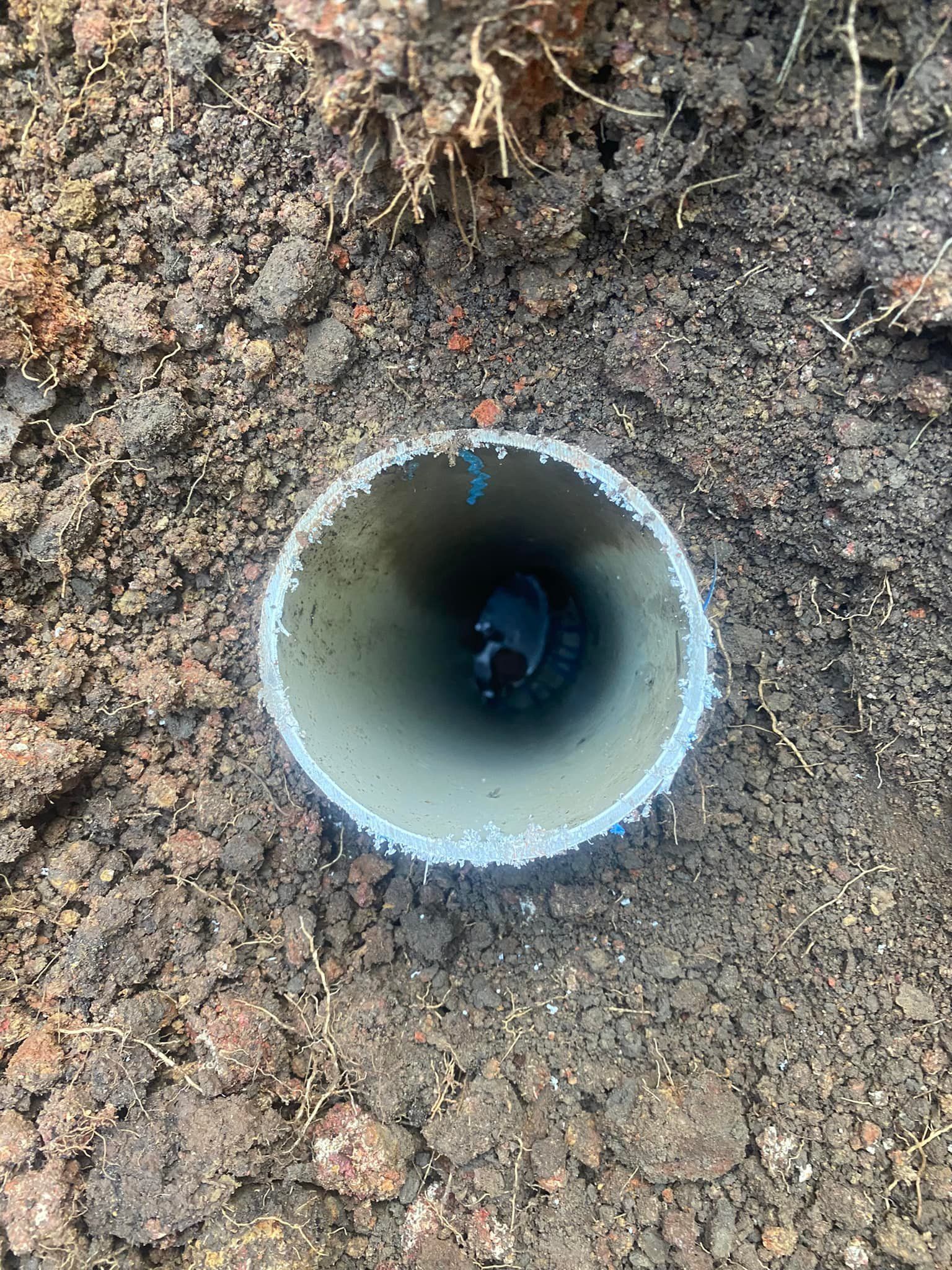 PVC Pipe in The Ground, Viewed from Above, Surrounded by Dark Soil — Medowie Plumbing & Gas in in Maitland