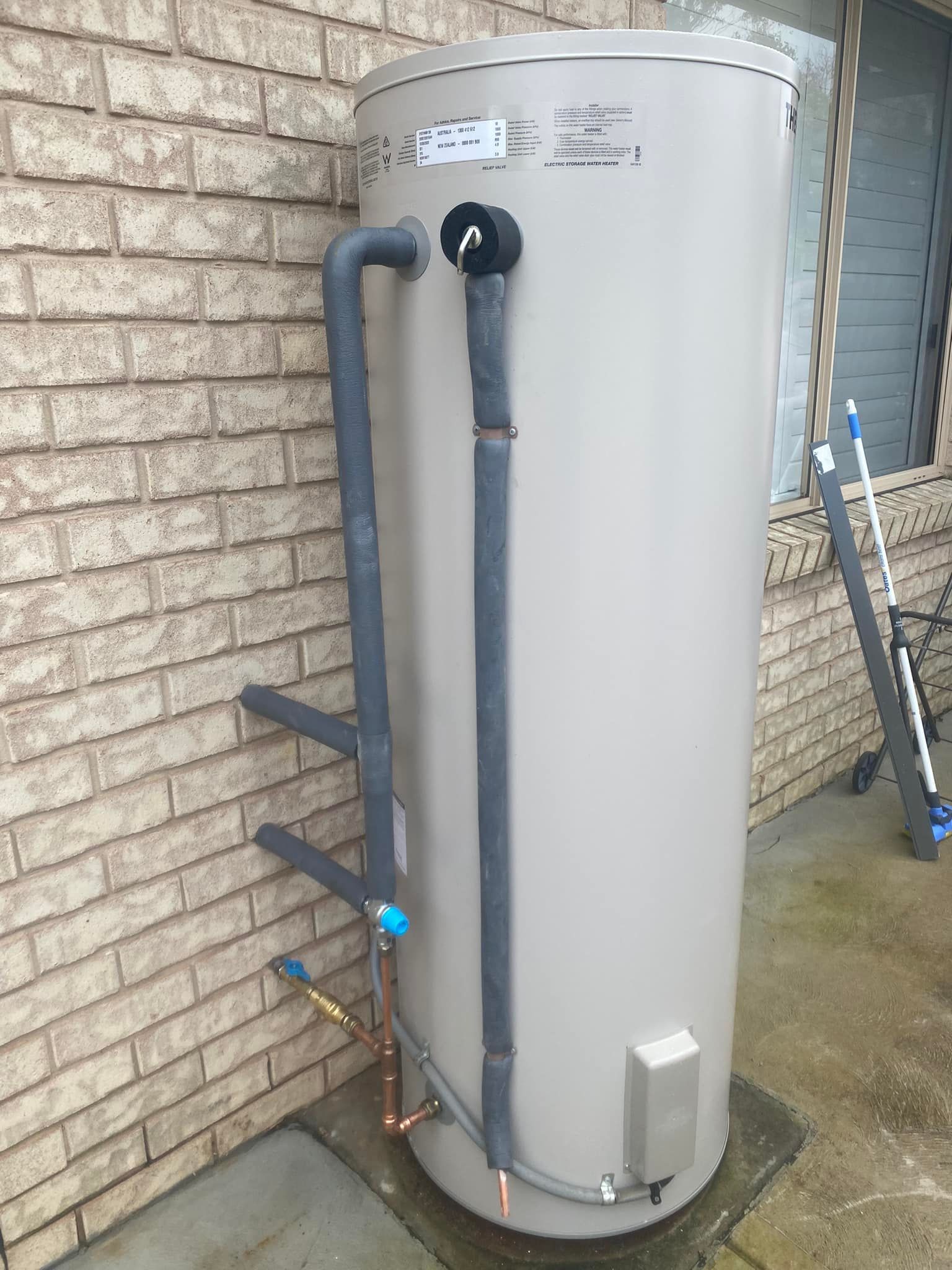 Tan Water Heater Tank Outdoors Against a Brick Wall — Medowie Plumbing & Gas in in Maitland