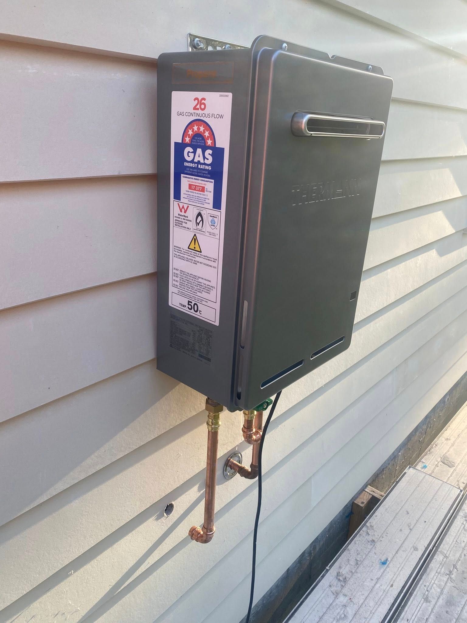Grey outdoor utility box mounted on house siding with a sign and cables underneath — Medowie Plumbing & Gas In Medowie, NSW