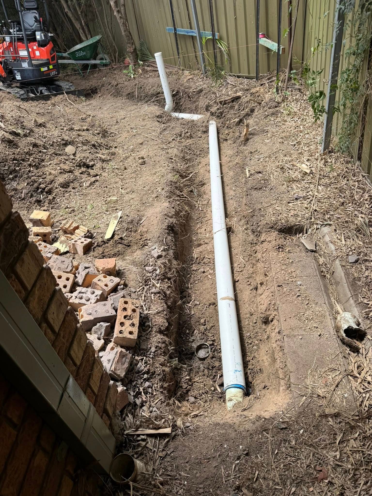 A Trench Dug in Dirt, with White Pipe Laid Inside, Near a Brick Wall — Medowie Plumbing & Gas in in Newcastle
