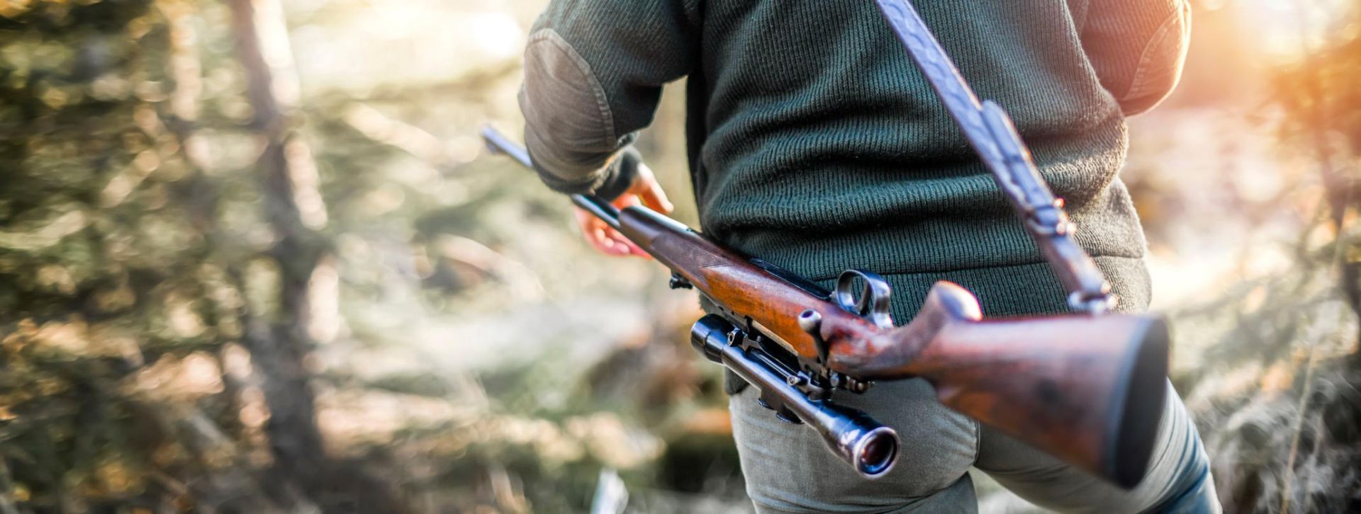 A Man Holding a Rifle Stands Among Trees — Coffs Coast Firearms In Inverell, NSW