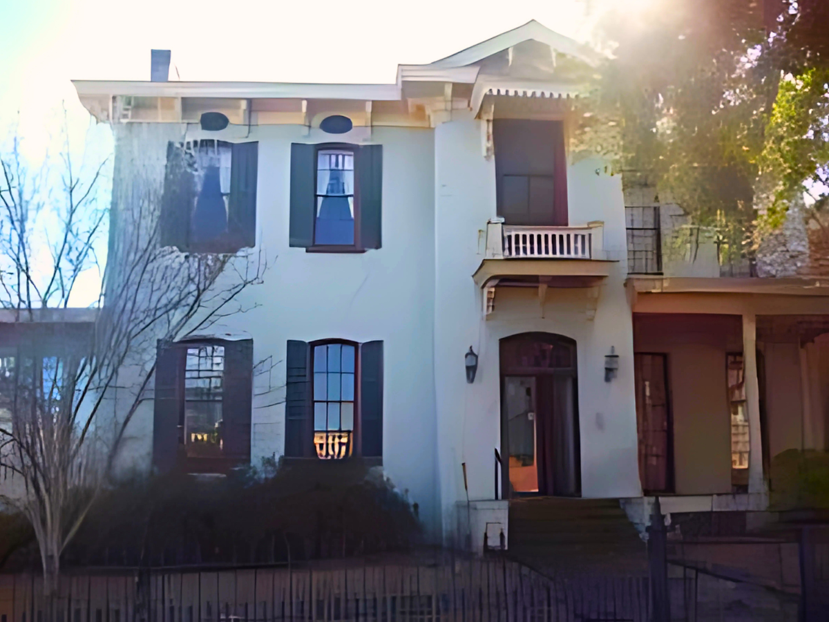 A large white house with black shutters and a balcony.