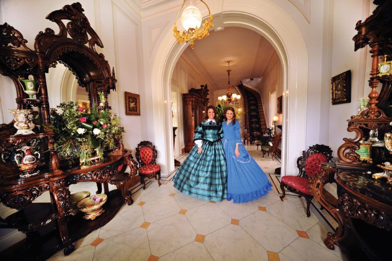 Two women in historical costumes are standing in a hallway