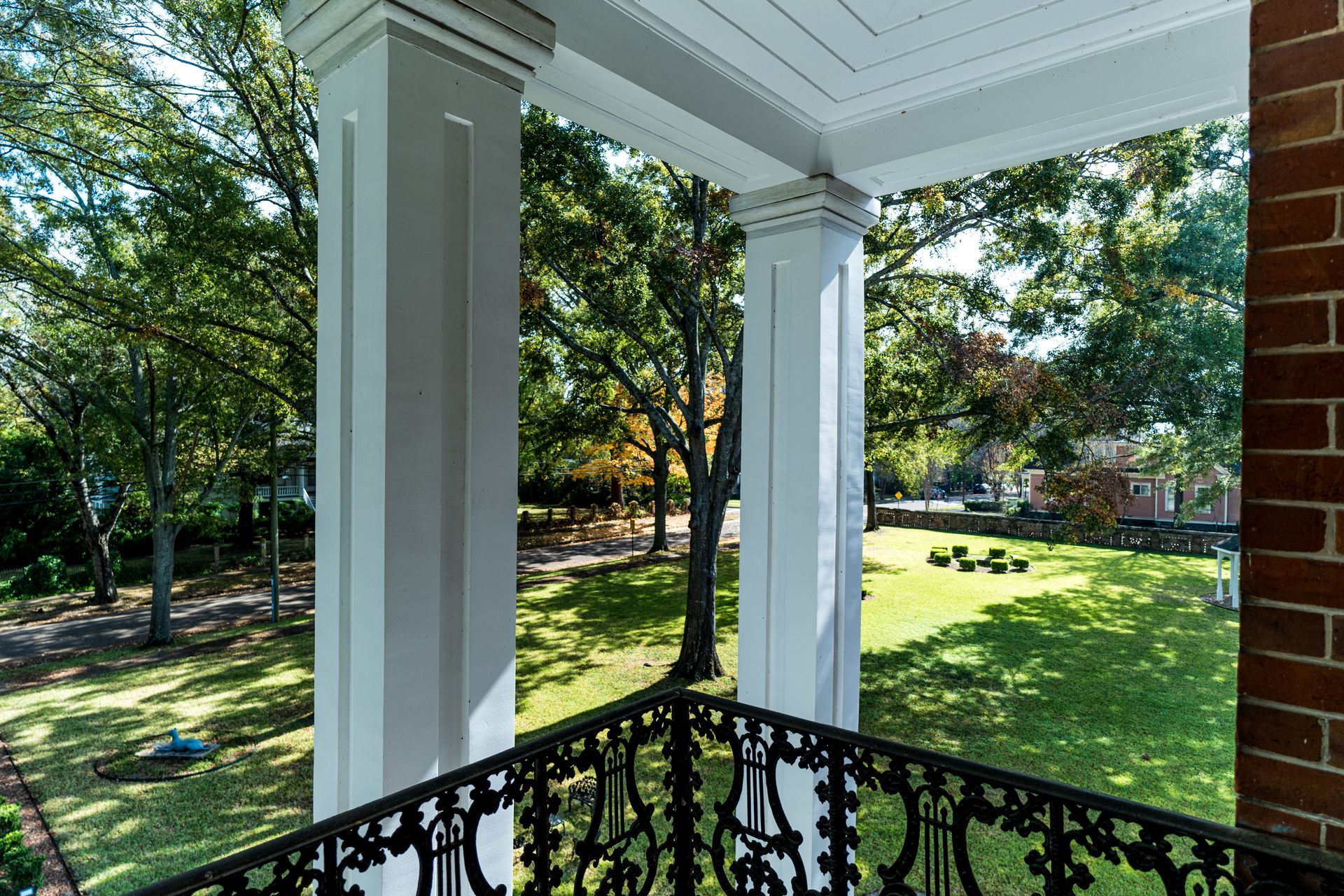 A porch with columns and a wrought iron railing overlooking a lush green field.