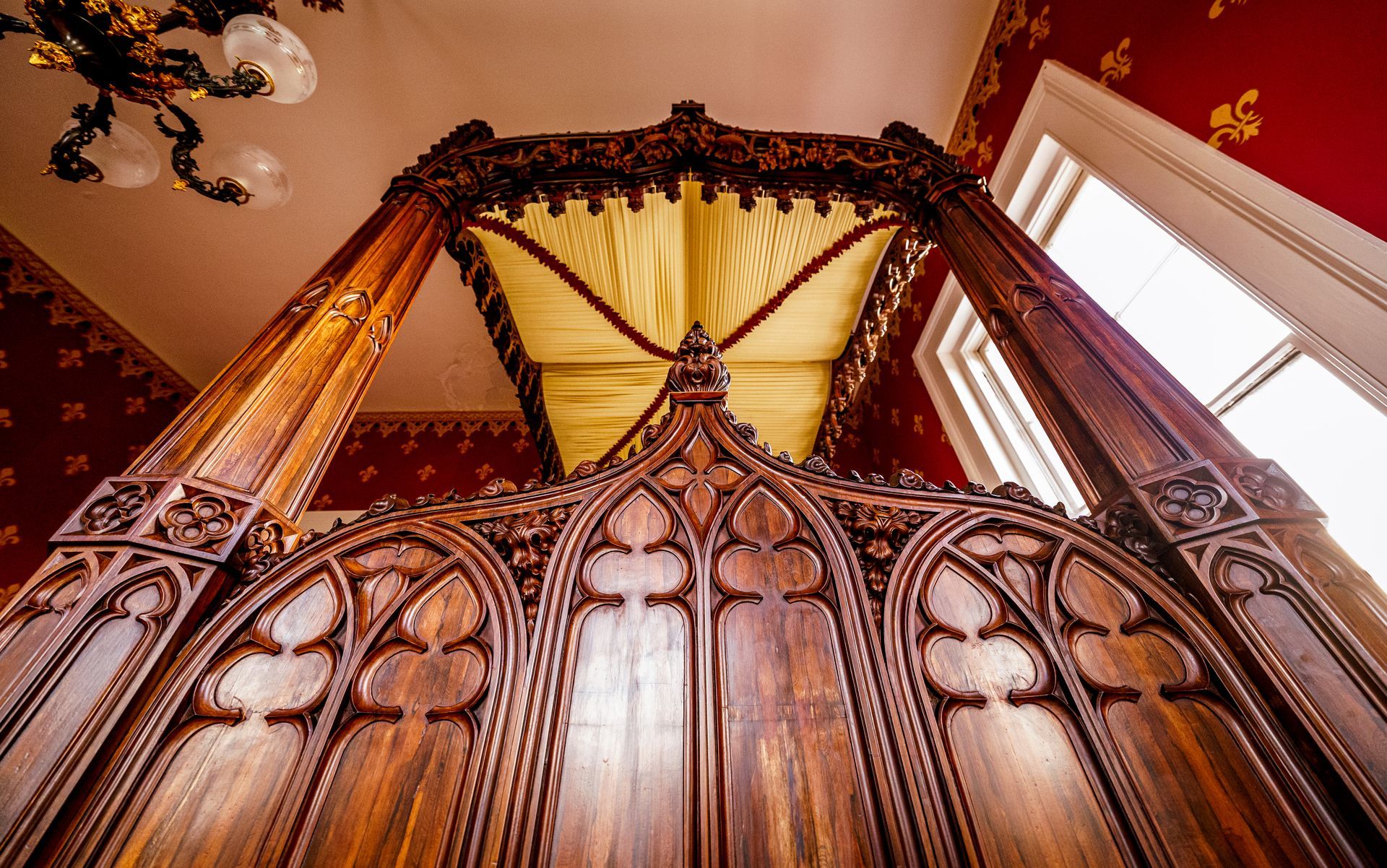 Looking up at a wooden canopy bed in a room with red walls.