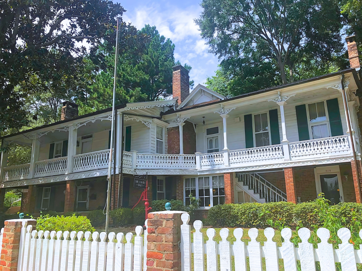 A large white house with green shutters and a white picket fence.