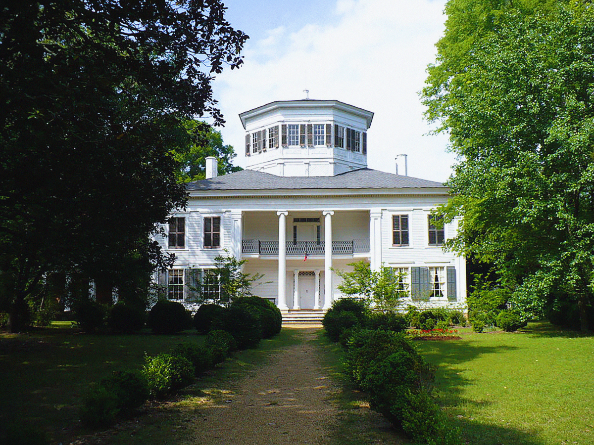 A large white house is surrounded by trees and bushes