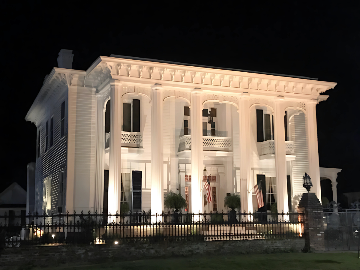 A large white house with columns is lit up at night.