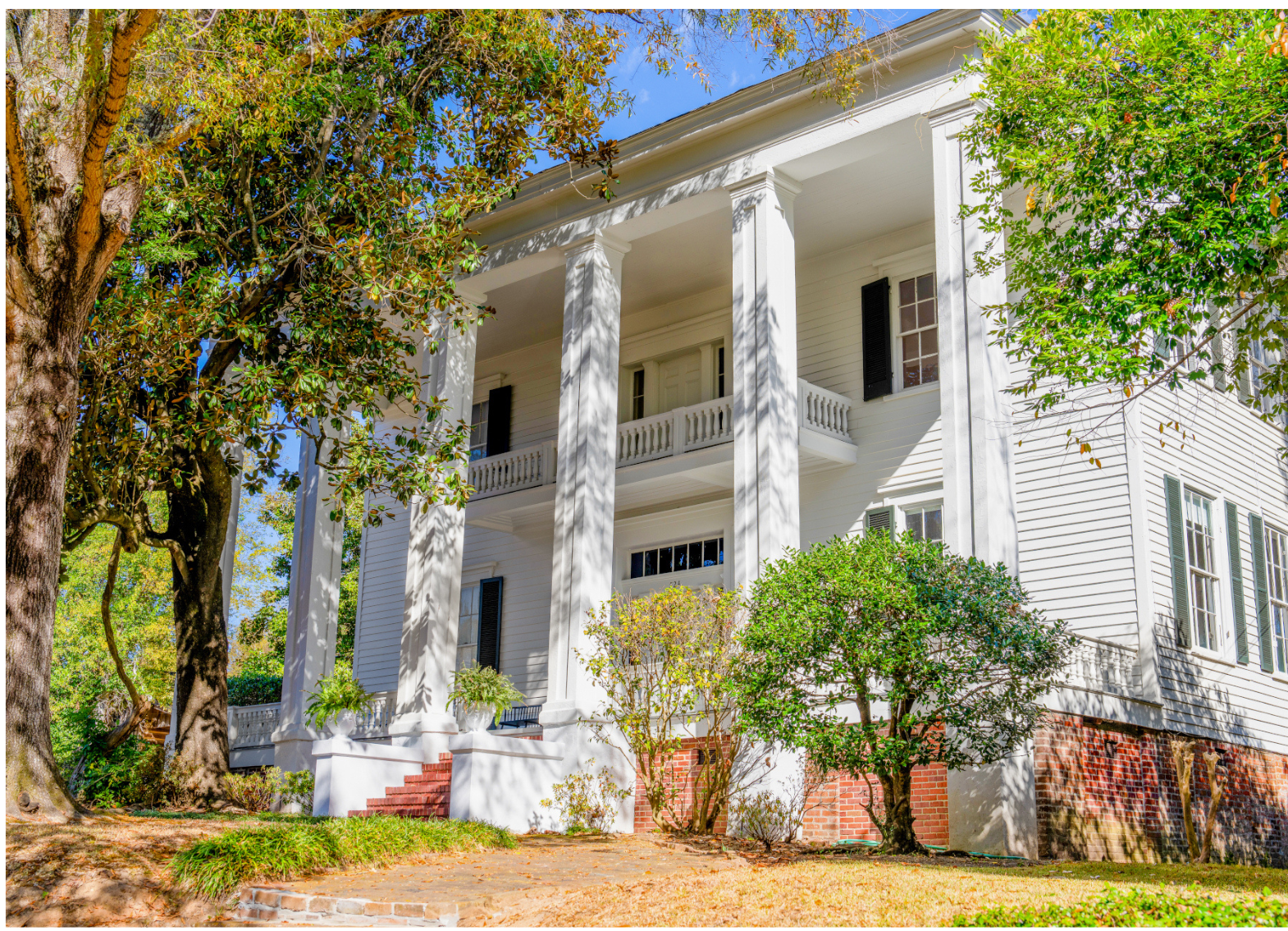 A large white house with columns and a porch surrounded by trees.
