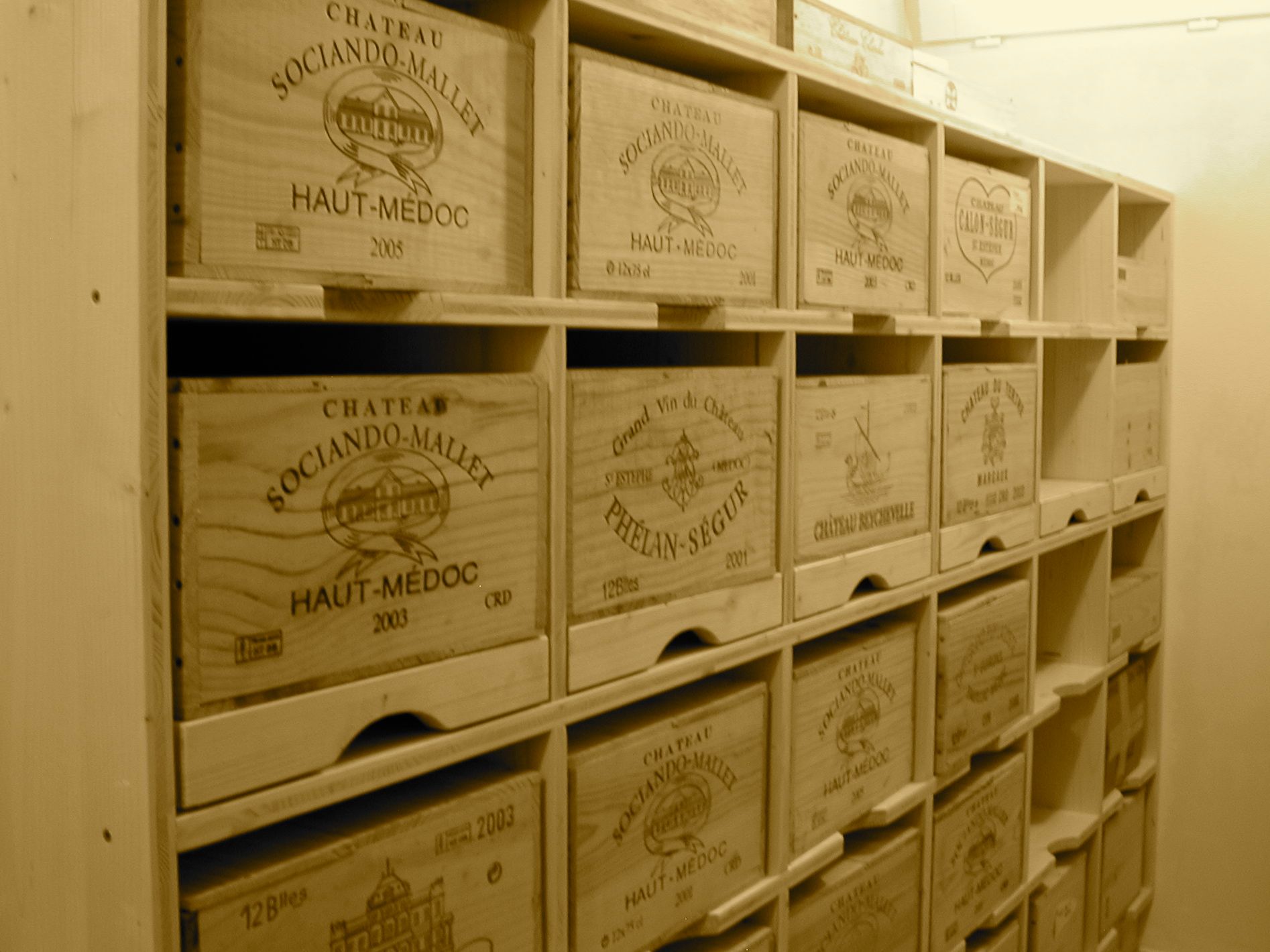 Caisses à vin en bois dans un casier de rangement, étiquetées avec les noms des vignobles, remplissant une cave.
