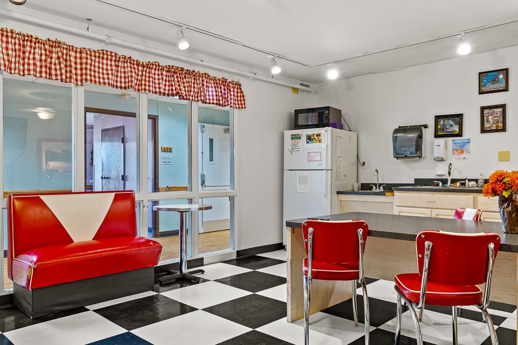 Retro diner-style break room with red booths, chairs, and checkered floor. Kitchen area with fridge and microwave.