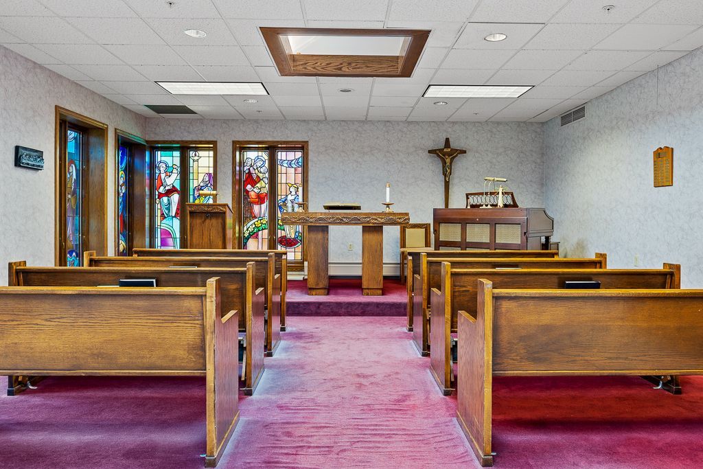 Interior view of a chapel with wooden pews, stained glass windows, and a crucifix.