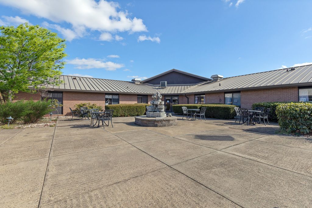 Exterior of a Quality Life Services brick building with a courtyard, fountain, and clear sky.