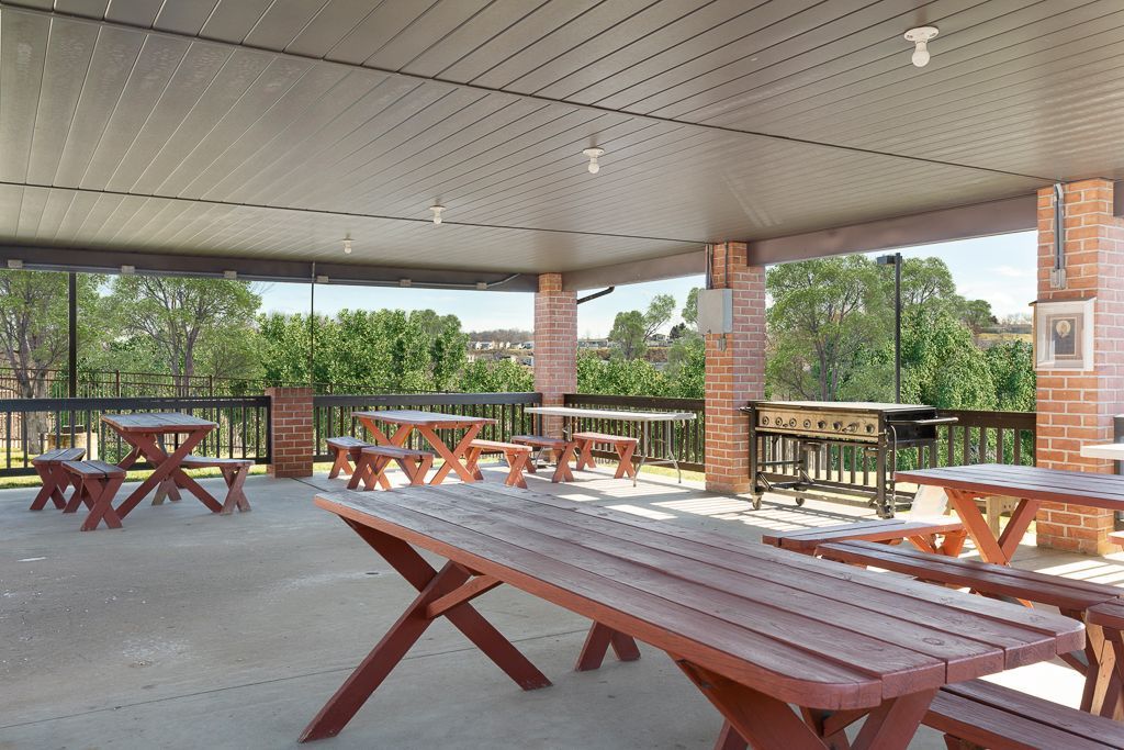 Outdoor covered patio with picnic tables, brick columns, and a view of trees.