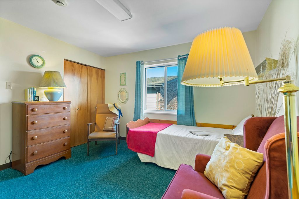 Bedroom with teal carpet, wooden furniture, and a bed.