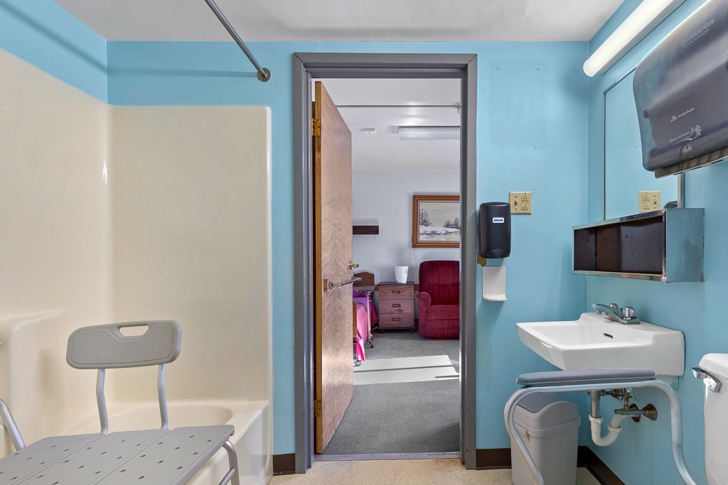 Bathroom with accessible features: shower chair, low sink, open doorway to living space. Blue and beige.