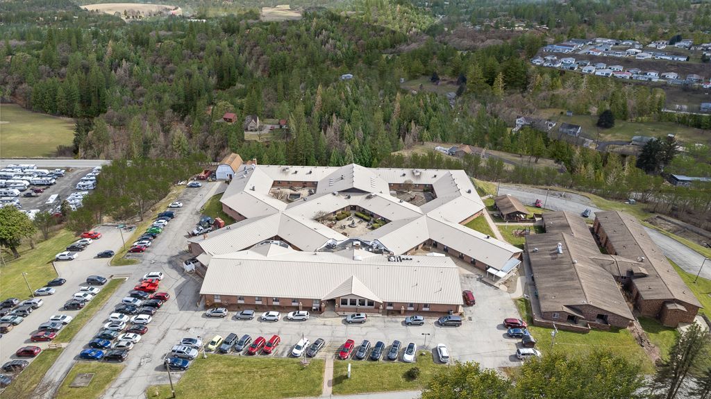 Aerial view of a large, complex building with multiple wings, surrounded by parking lots and trees.