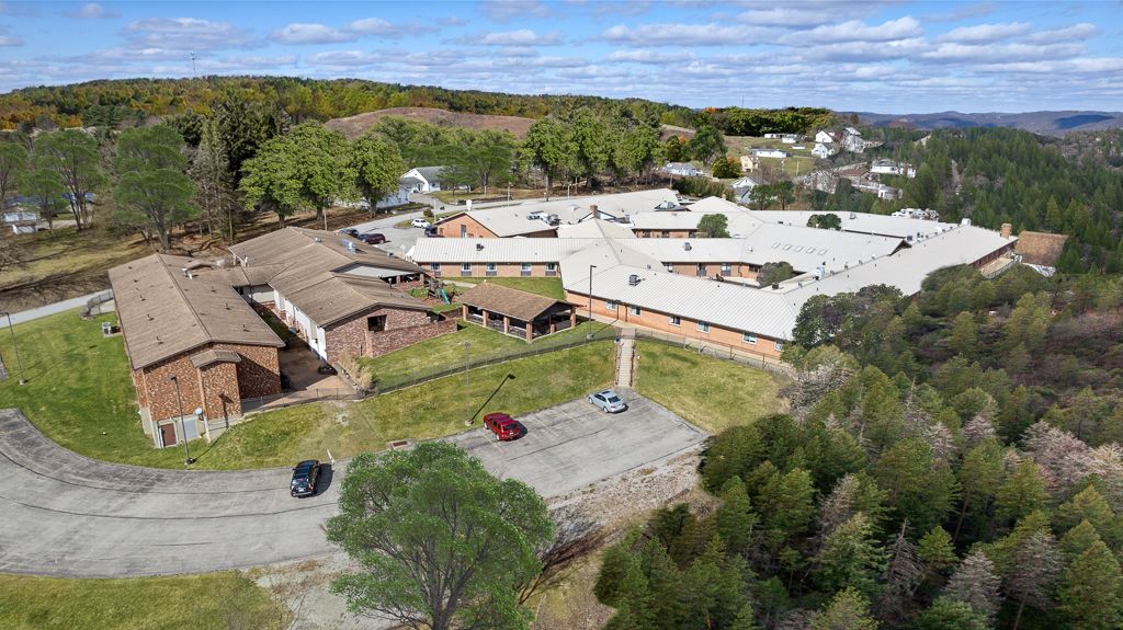 Aerial view of a large brick building complex with multiple wings, surrounded by trees and hills.