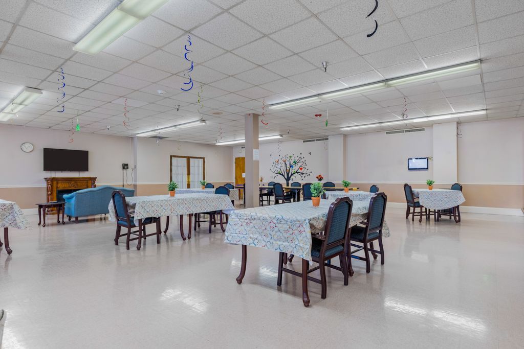 A brightly lit, empty dining hall with tables set for meals, a blue sofa, and a fireplace.