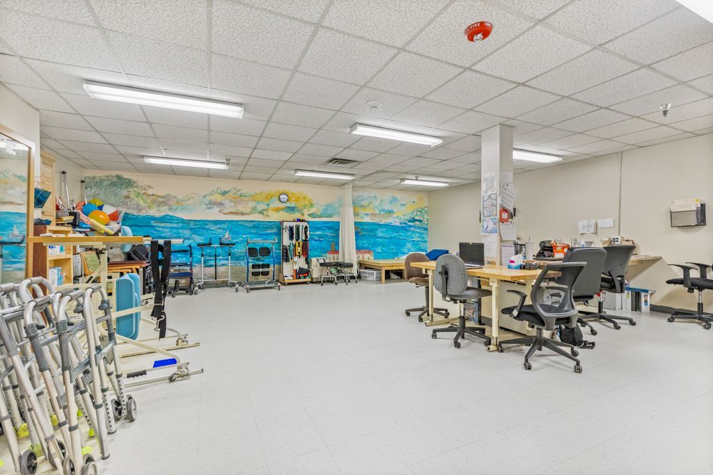 A physical therapy room with exercise equipment, desks, and a wall mural.