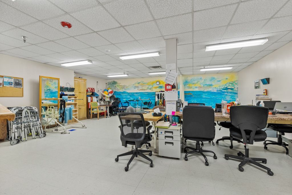 Office space with desks, chairs, artwork on walls, and fluorescent lights.
