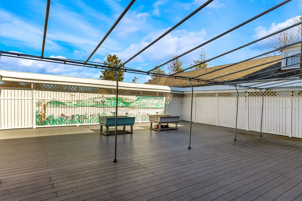Outdoor patio with gray flooring, tables, white fencing, and a wire canopy under a blue sky.