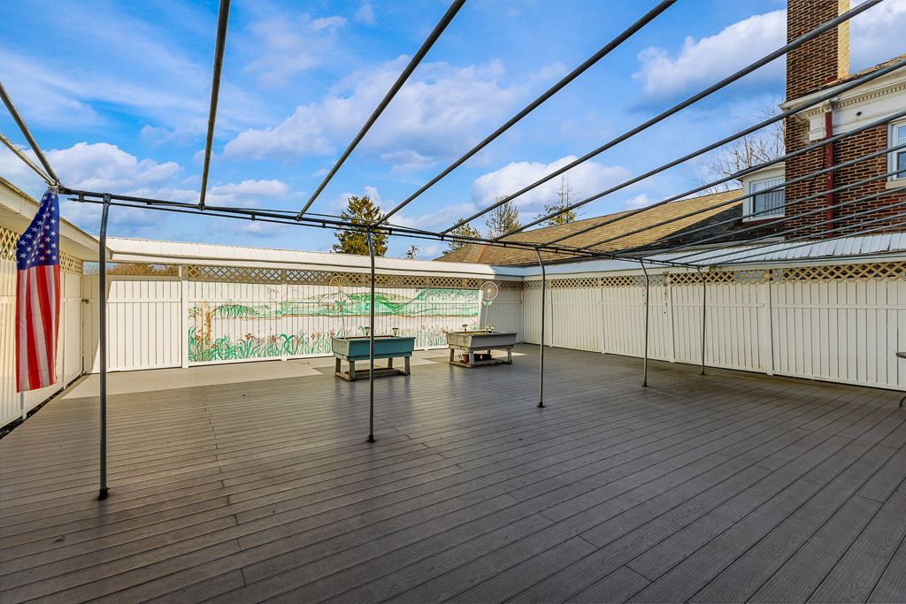 Large outdoor patio with overhead supports, two tables, American flag, and white curtains.