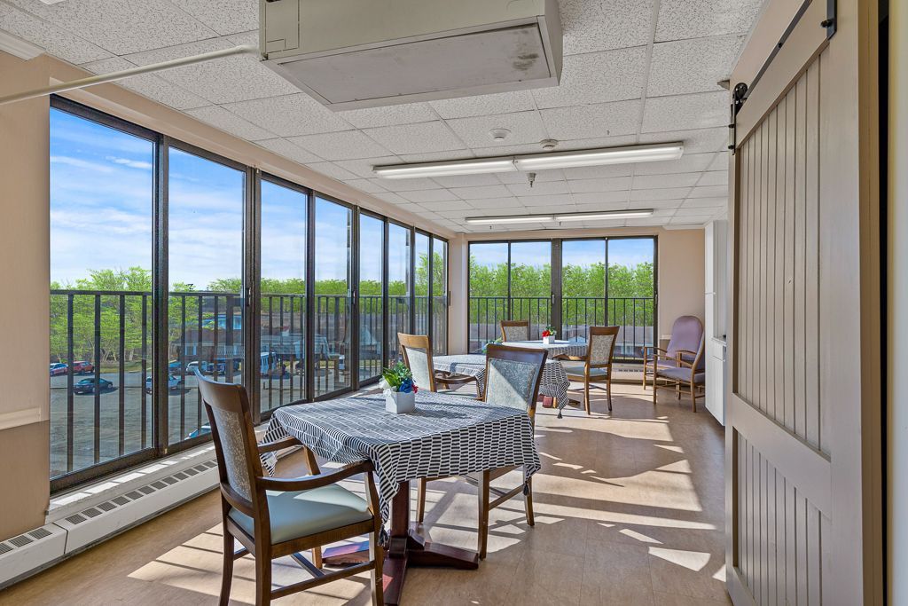 Sunroom with tables, chairs, and large windows overlooking trees. A barn door on the right.