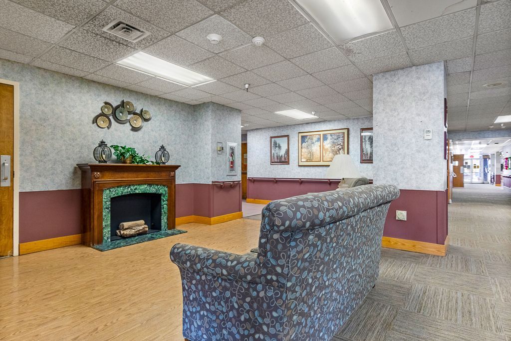 Interior of a senior living common area with a fireplace, couch, and hallway.