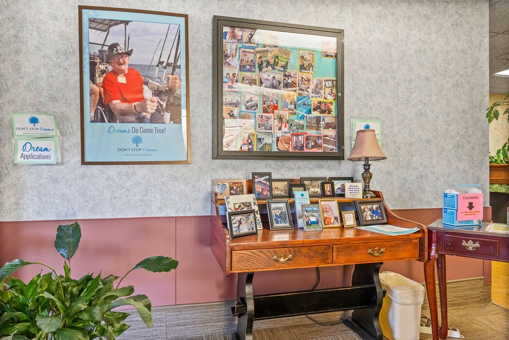 Desk with photos and framed art on a wall, potted plant in front, lamp, and pink wainscoting.