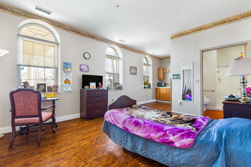 Bedroom with arched windows, bed, dresser, desk, and view of the kitchen and bathroom.