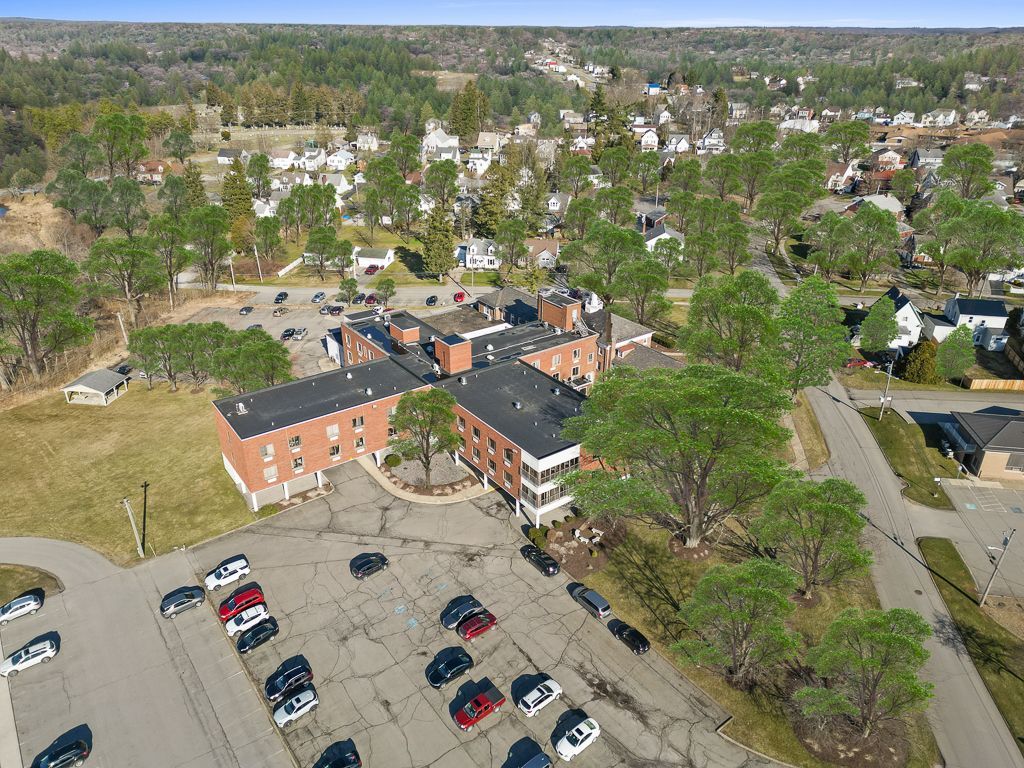Aerial view of a multi-story brick building with a parking lot and surrounding trees, in a residential area.