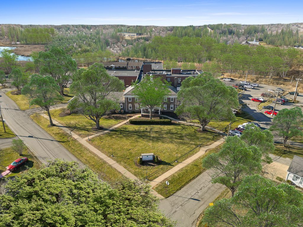 Aerial view of a large brick building surrounded by trees and a parking lot. Brown and green landscape with a road.