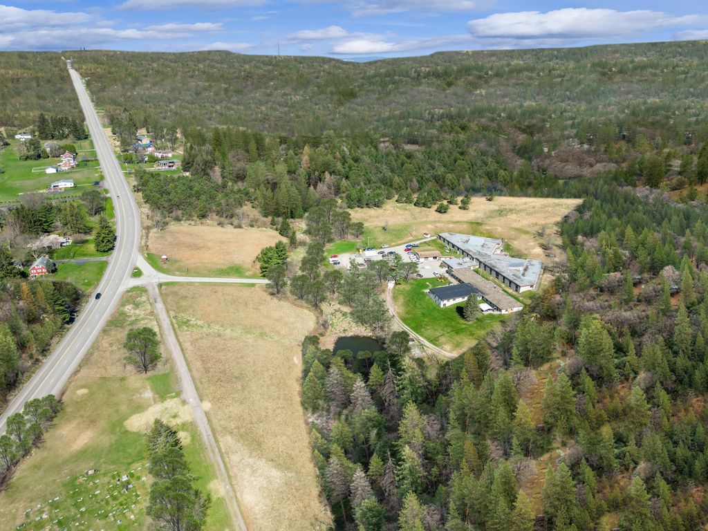 Aerial view of a long road through a forest and field, leading to a building complex.