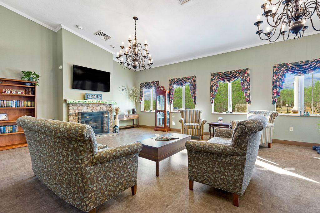 Living room with patterned armchairs, fireplace, windows, and chandeliers.