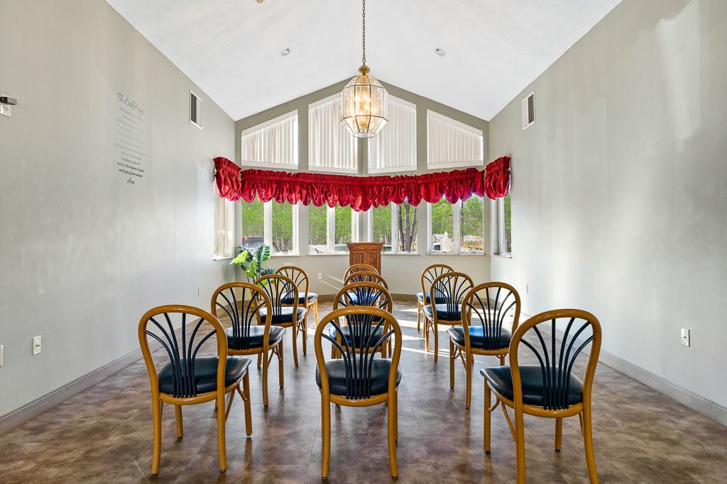 An empty room with arched ceiling, chairs in a circle, red valance, and large window.