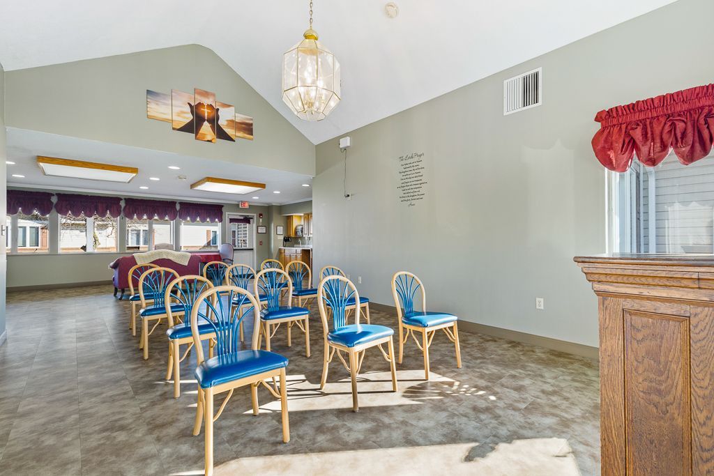 Empty chapel with blue chairs, a wooden podium, and a chandelier.