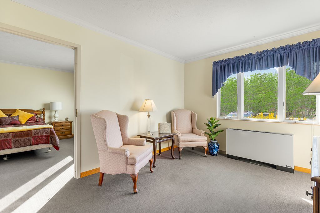 Living room with two pink armchairs, a table, and a window with blue curtains; bedroom visible in the doorway.