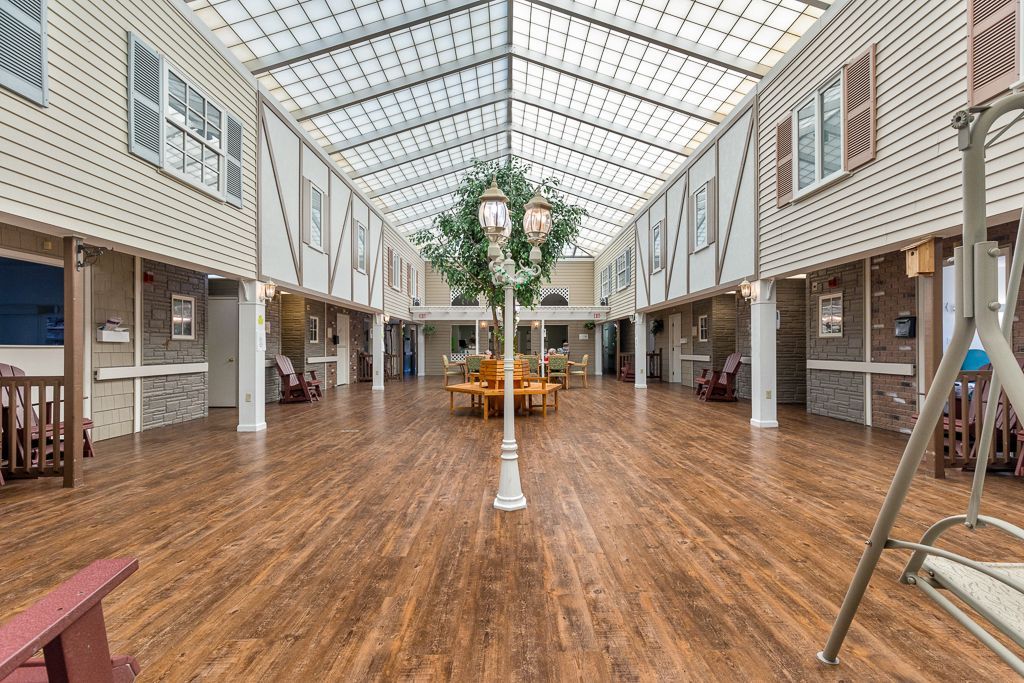 Bright, sunlit hallway in assisted living facility with wood floors, glass ceiling, and a faux tree centerpiece.