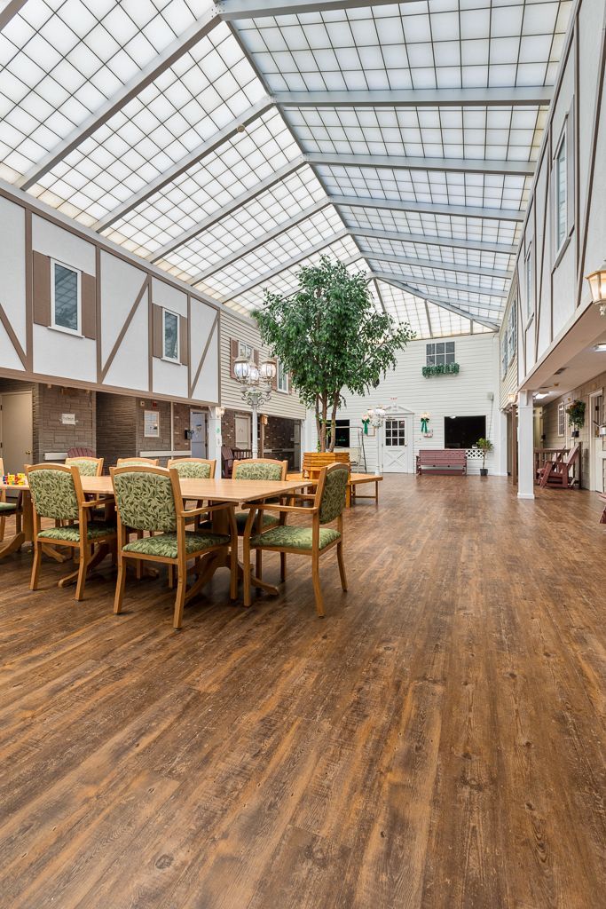 Spacious interior with glass roof, dining table with green chairs, and large tree.
