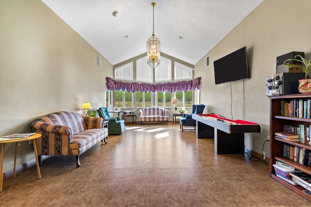 Spacious room with couches, a TV, and a bookshelf. Large windows, chandelier, and a piano.