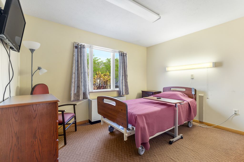 Hospital room with a bed, TV, and window; tan walls and carpet.