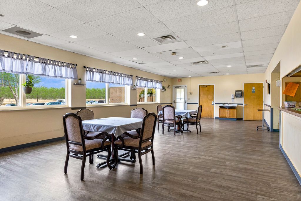 Dining room with round tables, chairs, windows, and neutral-colored walls and floor.
