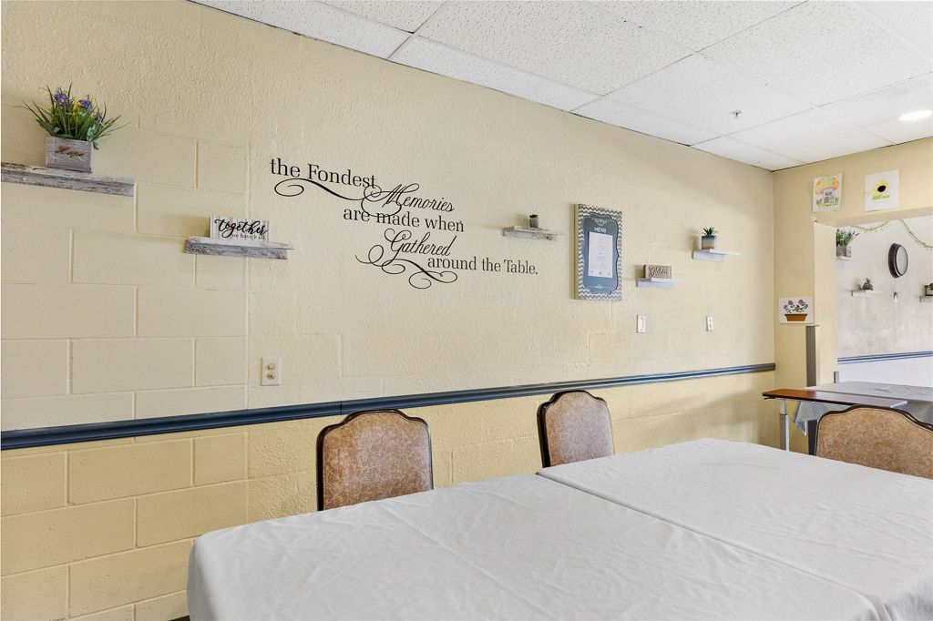 A dining room with tables, chairs, and a decorated wall; the wall has shelves and a quote.