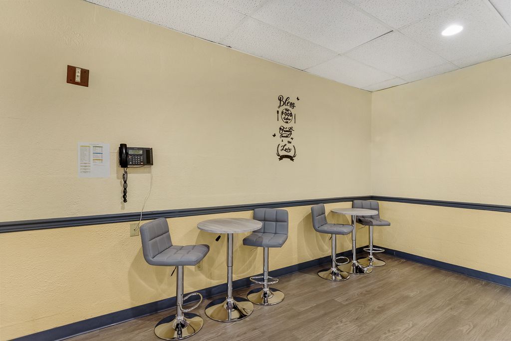 A small room with four bar stools and tables. Beige walls, light wood floor, and a phone are visible.