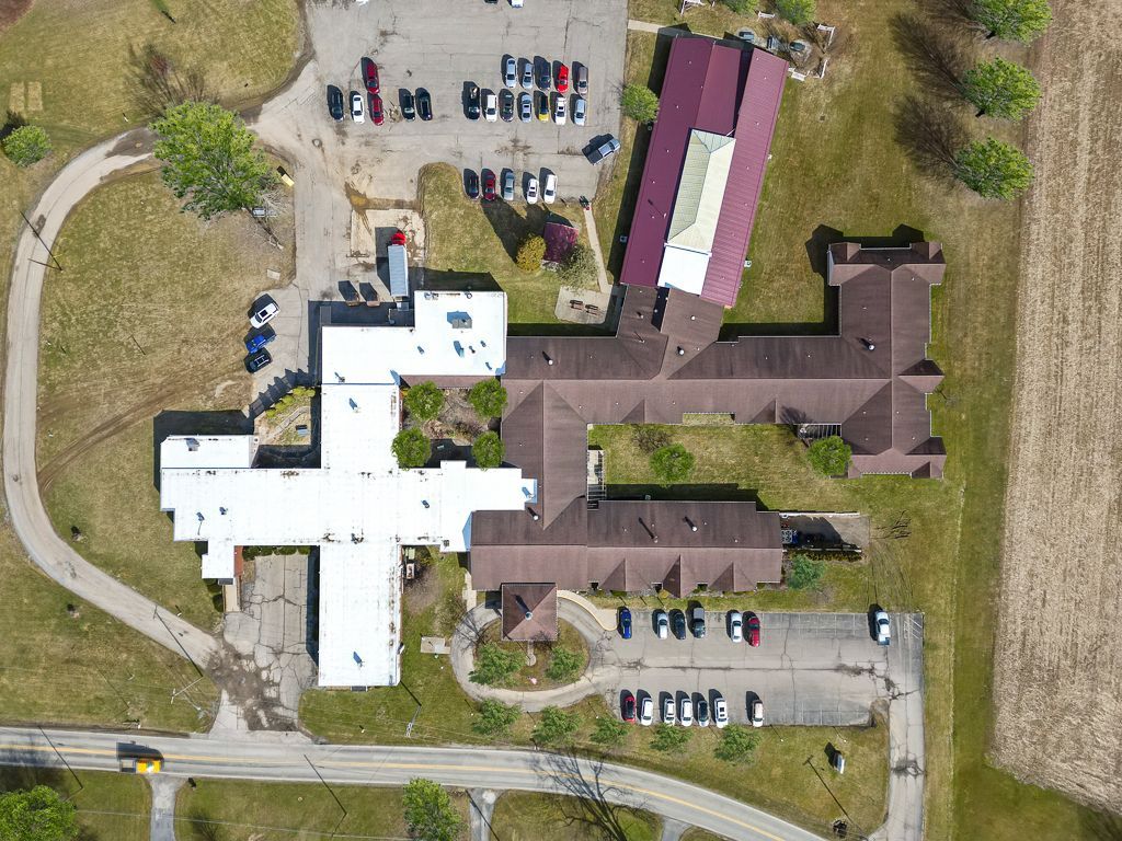 Aerial view of a brown and white building with a cross-like shape, surrounded by parking lots and fields.