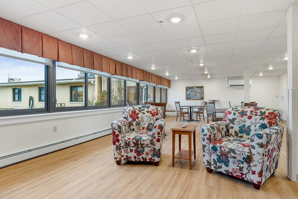 Spacious lounge with floral armchairs, large windows, and a small table.