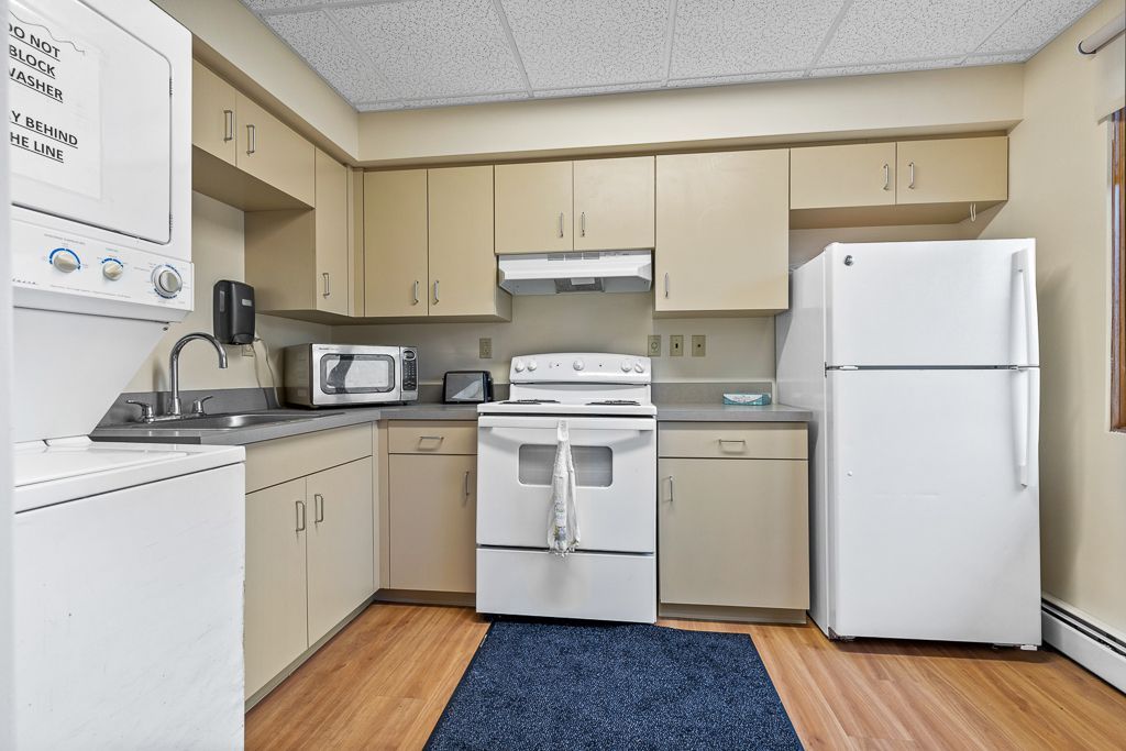 Kitchen with light-colored cabinets, white appliances, and a blue rug on a wood floor.